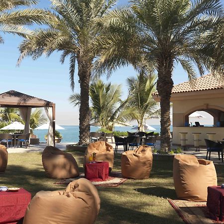 알 라하 비치 호텔 아부다비 레스토랑 사진 The photo depicts a beautiful outdoor setting with several elements of relaxation and leisure. In the foreground, there are large, comfortable bean bag chairs arranged on a grassy area, accompanied by low tables. Surrounding this seating area are tal