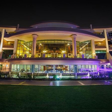 알 라하 비치 호텔 아부다비 외부 사진 The photo shows a modern architectural building illuminated at night. The structure has a large central entrance with multiple glass windows, flanked by symmetrical columns. The exterior features a combination of sleek lines and curves, with lighting