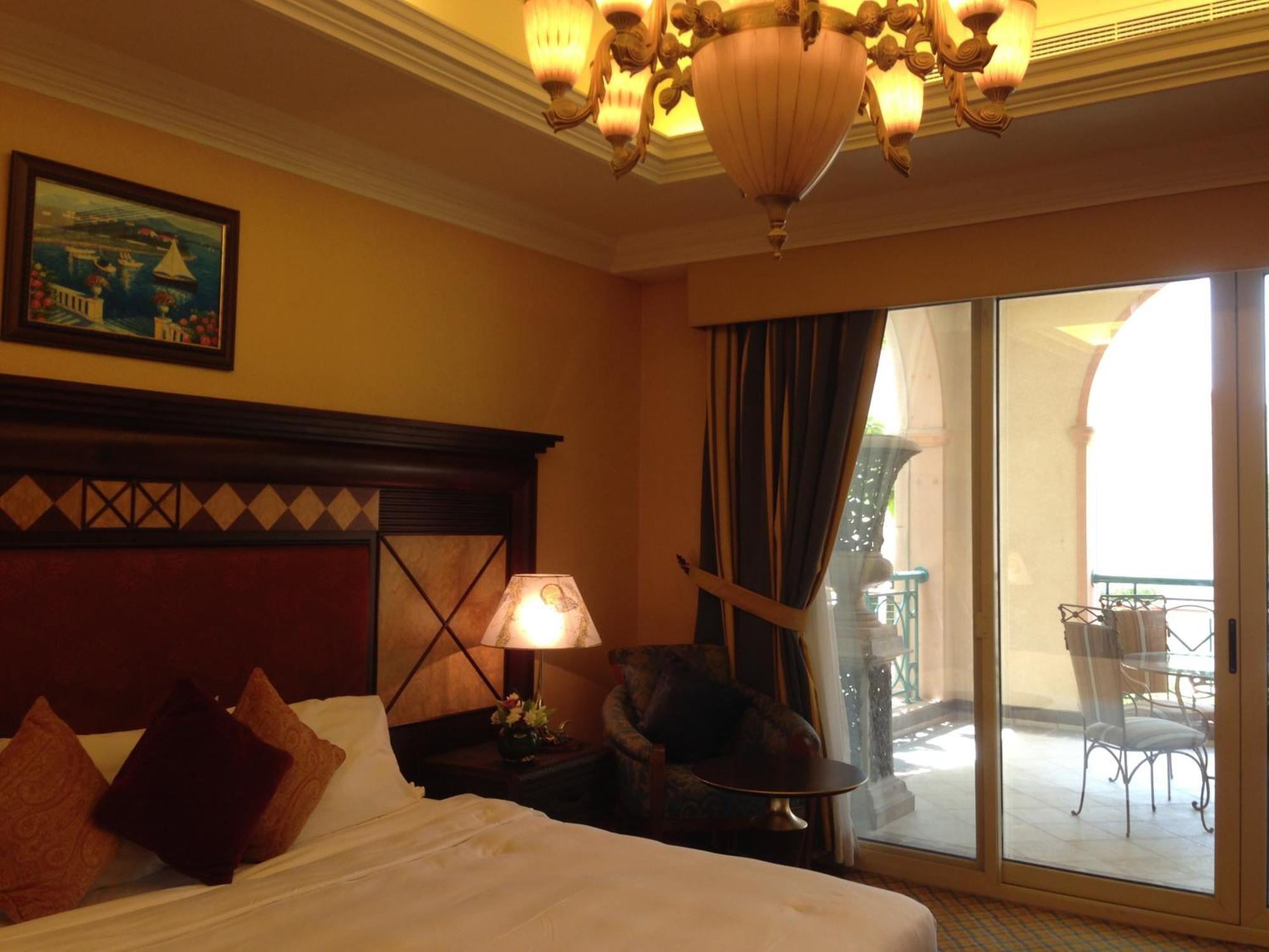 알 라하 비치 호텔 아부다비 외부 사진 The photo shows the interior of a hotel room. The room features a large bed with decorative cushions and a wooden headboard. There's a bedside lamp emitting a warm light, and a painting is hung on the wall above the bed. To the right, there's a windo