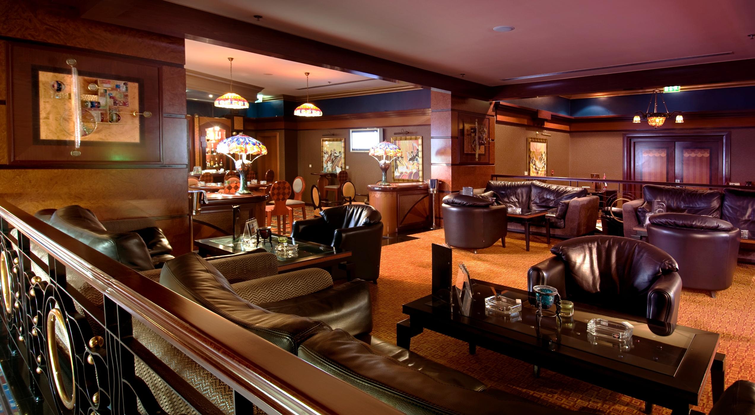 알 라하 비치 호텔 아부다비 내부 사진 The photo depicts a stylish lounge area featuring comfortable seating and an inviting atmosphere. There are several plush leather armchairs and sofas arranged around low tables. The space is well-lit, with stained glass lamps providing warm light. Th