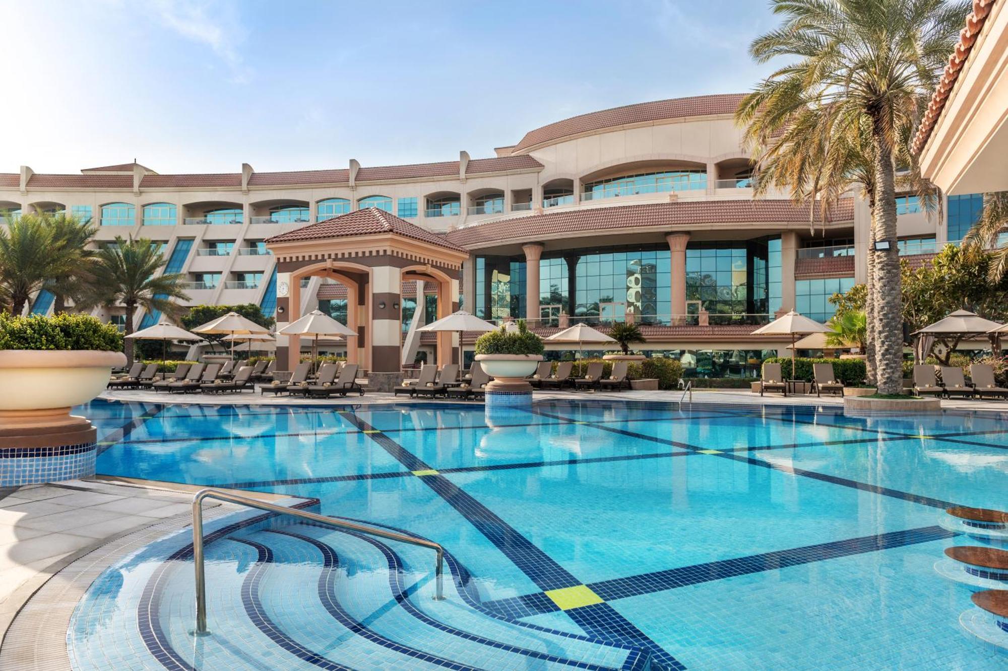 알 라하 비치 호텔 아부다비 외부 사진 The photo shows a luxurious resort with a large swimming pool in the foreground. The pool has a clean, blue surface and features lounge chairs on the surrounding deck. In the background, there is a stylish and modern hotel building with multiple stor