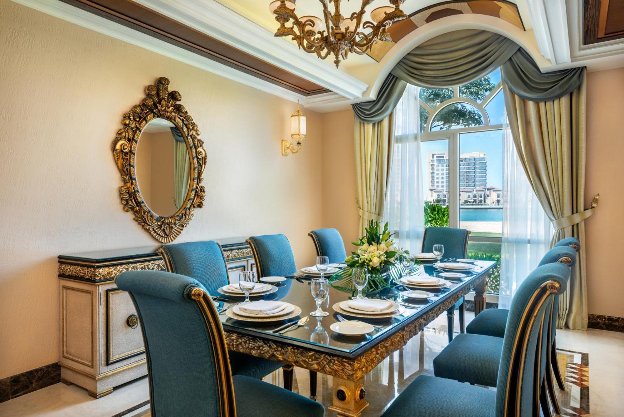 알 라하 비치 호텔 아부다비 외부 사진 The photo features an elegantly decorated dining room. It includes a long, polished table set for a meal with plates, glasses, and decorative items, surrounded by plush blue chairs. The room is adorned with sophisticated details, such as an ornate mi