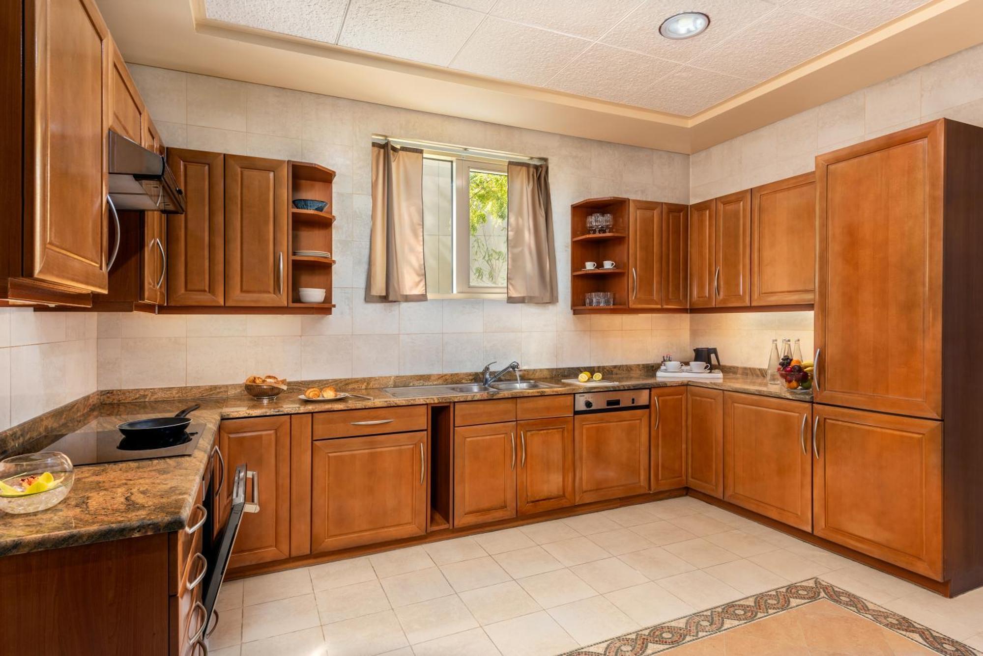 알 라하 비치 호텔 아부다비 외부 사진 The photo shows a cozy kitchen featuring wooden cabinets with a rich brown finish, providing a warm and inviting atmosphere. The countertops are made of a light-colored stone, complementing the cabinetry. There is a window above the sink, allowing na
