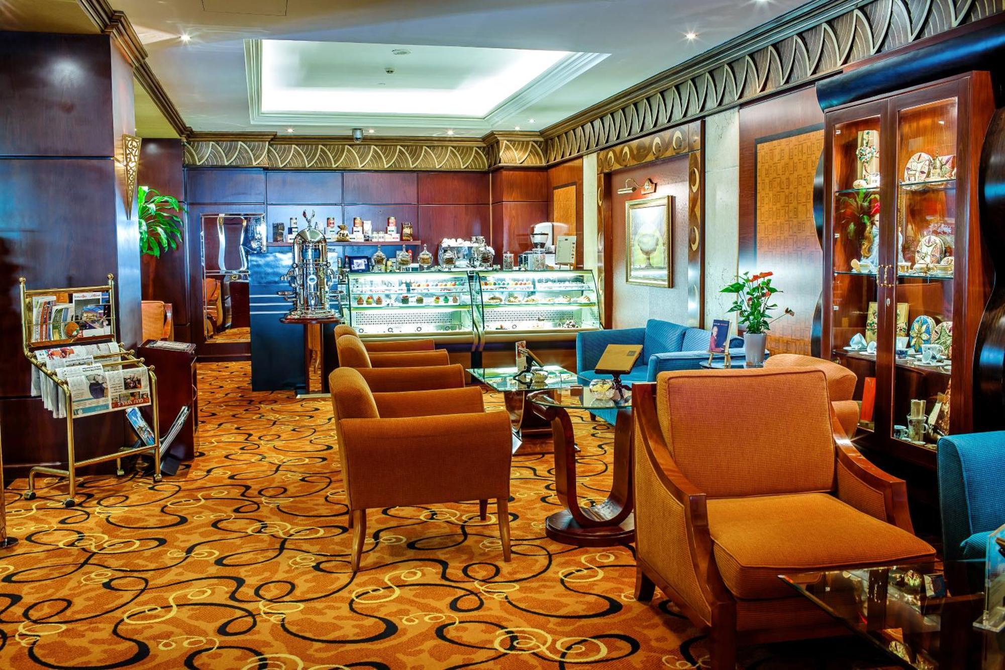 알 라하 비치 호텔 아부다비 외부 사진 The photo shows a cozy and elegantly designed lounge or café area. It features plush seating with brown armchairs and a blue couch. In the background, there is a display case filled with various items, likely including pastries or decorative goods. T