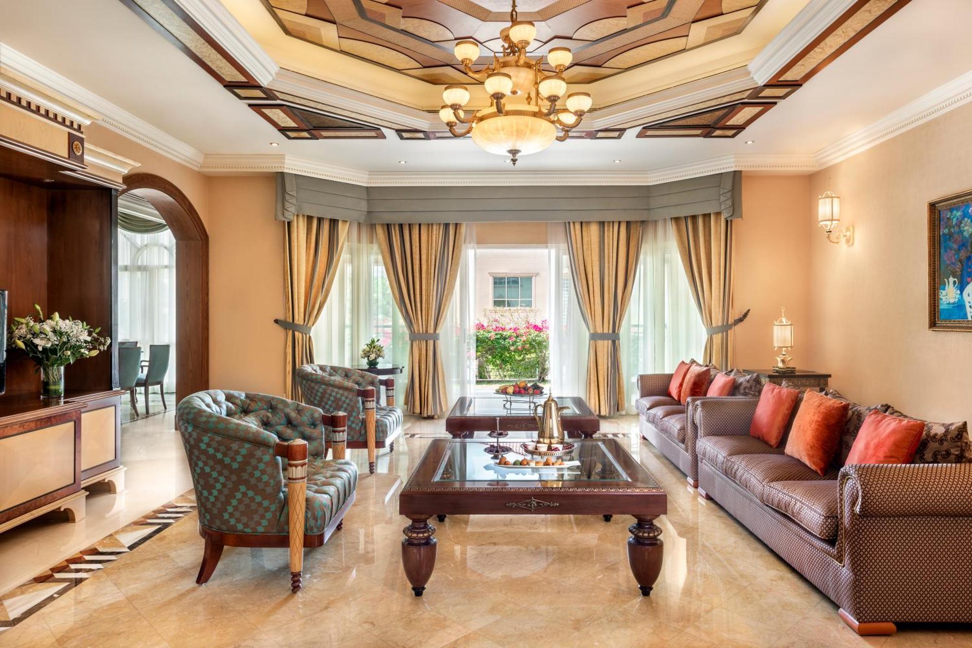 알 라하 비치 호텔 아부다비 외부 사진 The photo shows an elegantly designed living room. It features a high, intricately patterned ceiling with a chandelier hanging in the center. The room is filled with natural light from large windows covered with flowing curtains. 

There are two diff
