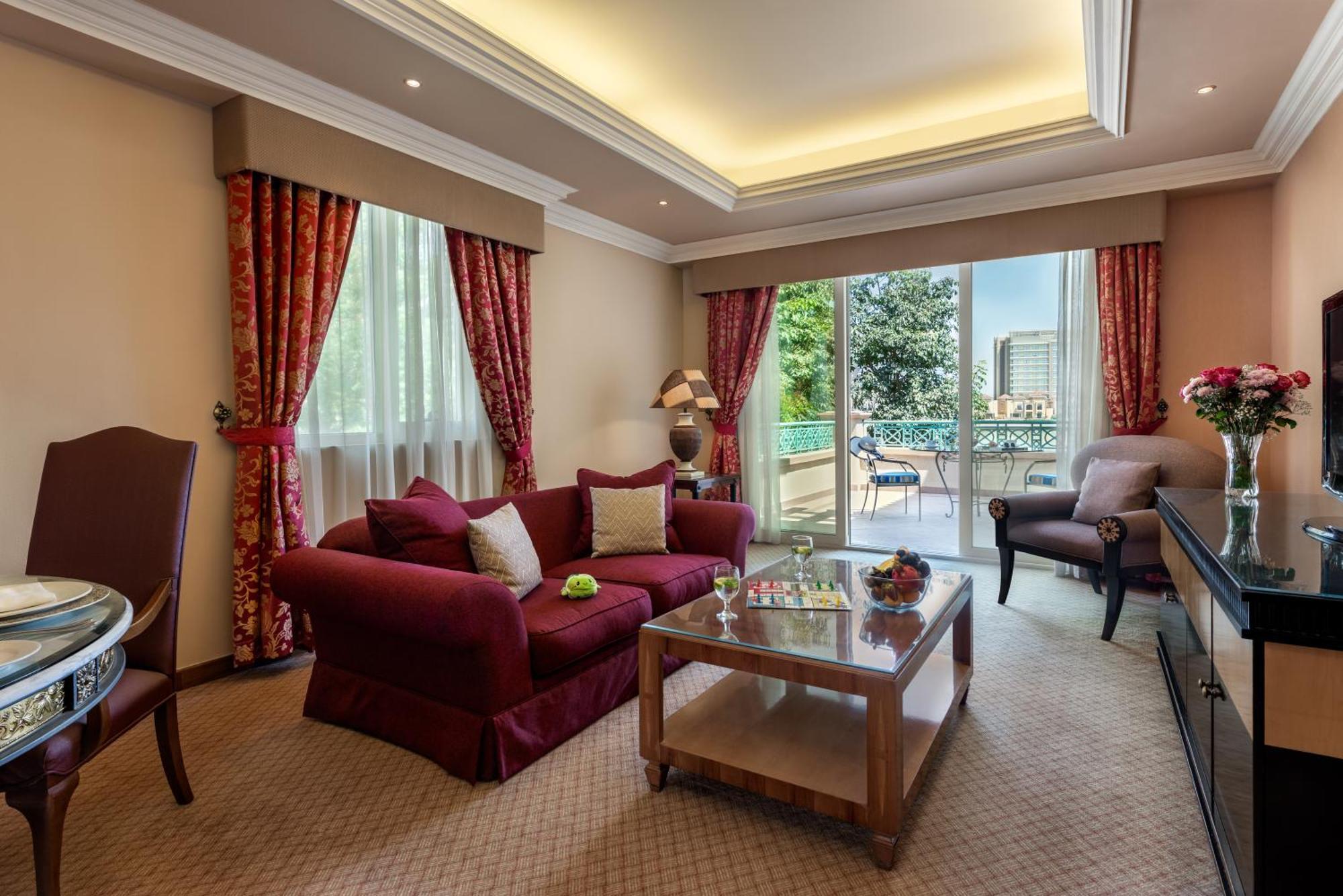 알 라하 비치 호텔 아부다비 외부 사진 The photo shows a well-decorated hotel room or living area. It features a cozy seating arrangement with a deep red couch adorned with cushions, paired with a single chair. There is a glass coffee table in front of the couch, which is set on a plush c