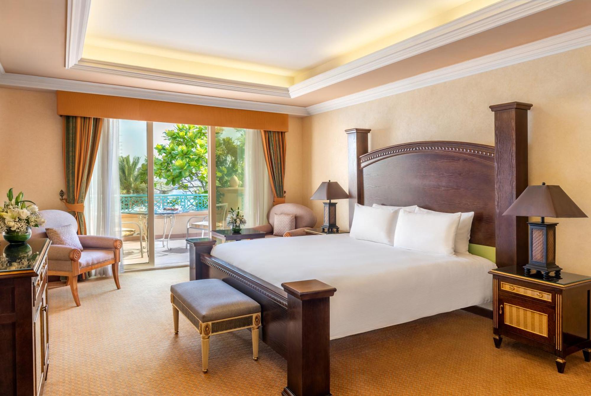 알 라하 비치 호텔 아부다비 외부 사진 The photo shows a well-appointed hotel bedroom. It features a large bed with white bedding, flanked by bedside tables with lamps. The room has light-colored walls and a warm-toned carpet. There is a comfortable seating area with a chair and a small t