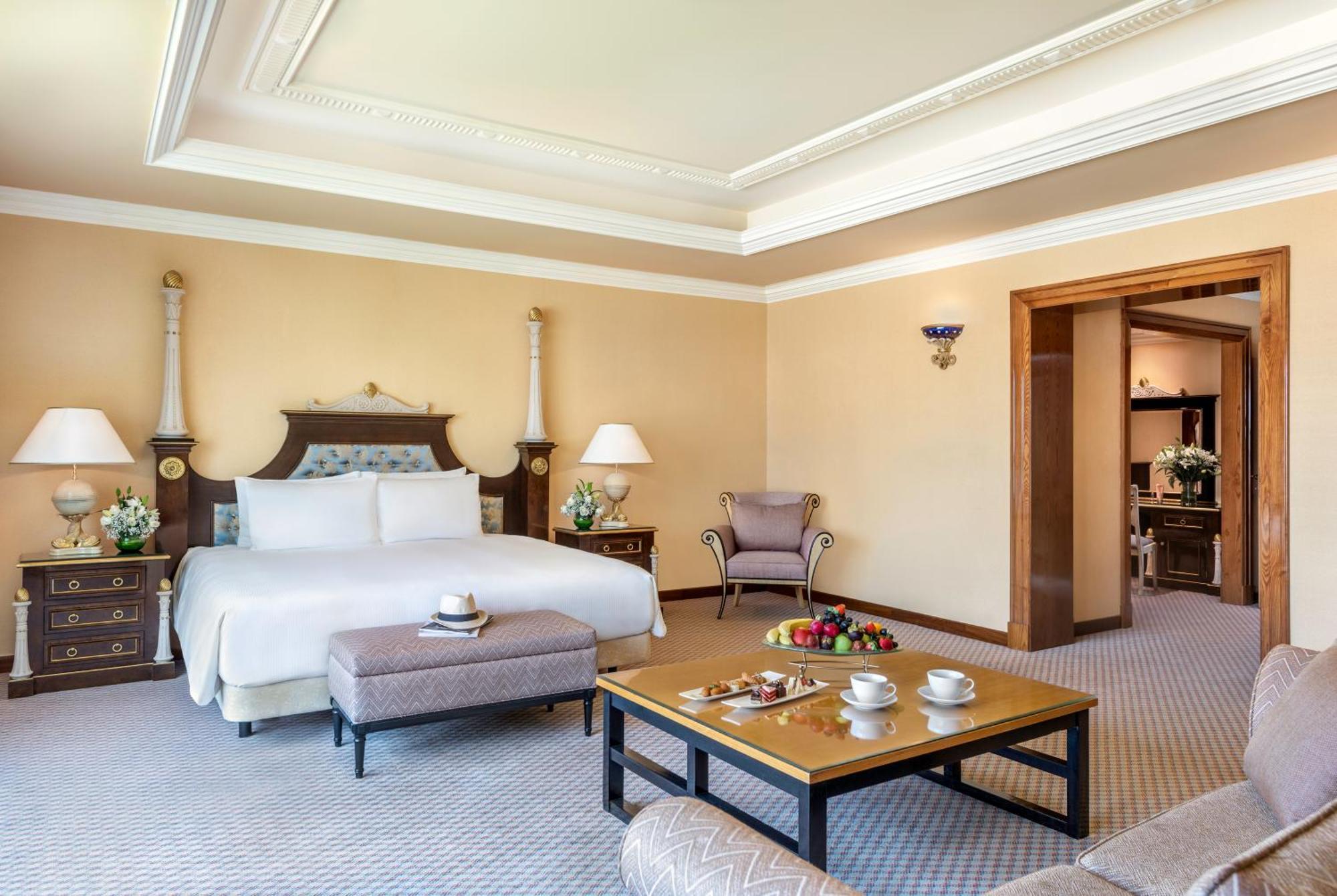 알 라하 비치 호텔 아부다비 외부 사진 The photo shows an elegant hotel room, featuring a large bed with white linens, flanked by stylish bedside tables and lamps. The room has a warm color palette, with light brown walls and a plush carpet. A comfortable armchair is positioned nearby, an