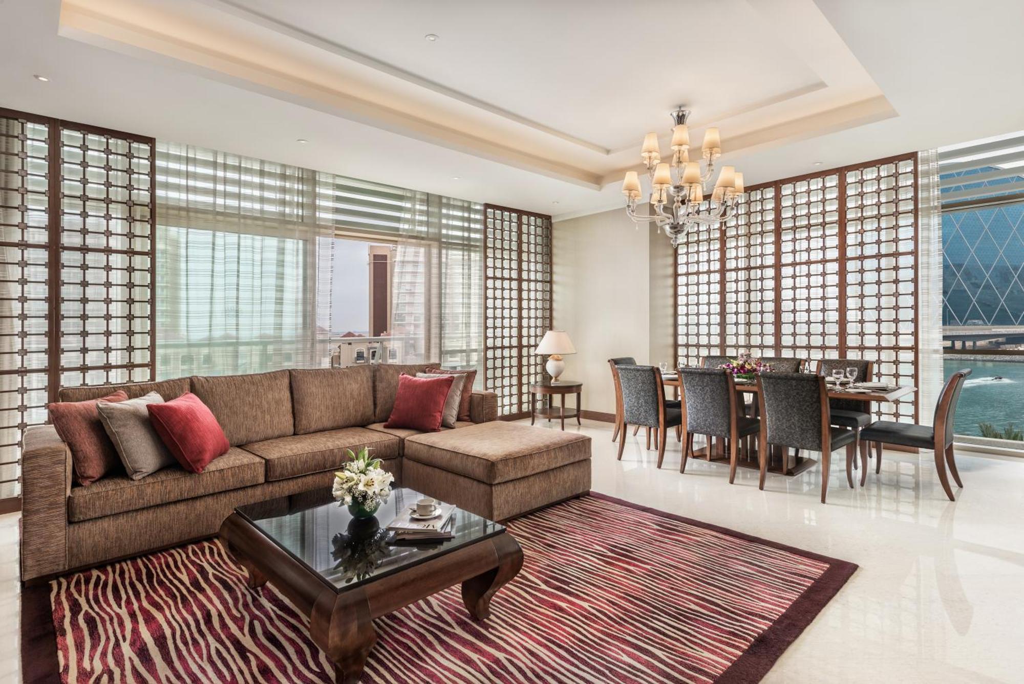 알 라하 비치 호텔 아부다비 외부 사진 The photo shows a stylish and modern living space. On one side, there is a comfortable sectional sofa in a brown upholstery, accented with red and gray cushions. In front of the sofa, there is a glossy black coffee table adorned with a small floral a