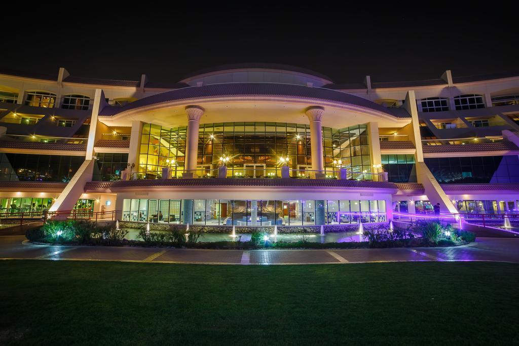 알 라하 비치 호텔 아부다비 외부 사진 The photo shows a modern architectural building illuminated at night. The structure has a large central entrance with multiple glass windows, flanked by symmetrical columns. The exterior features a combination of sleek lines and curves, with lighting